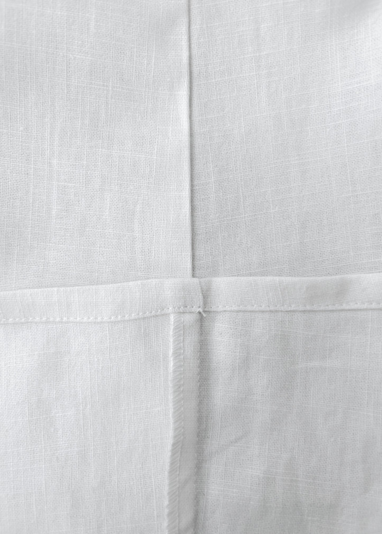 Close-up of white woven fabric with a visible cross-stitch pattern and fine linen texture.