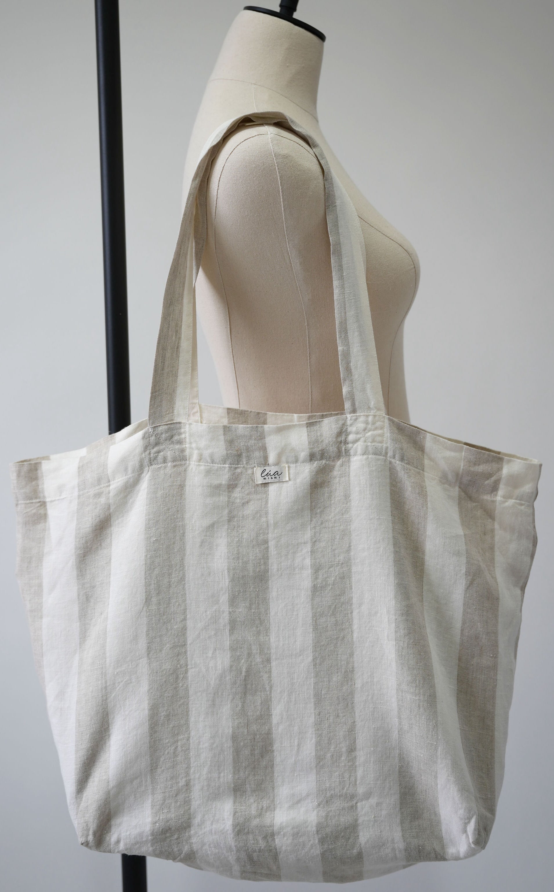 Natural linen tote bag, oversized, soft ivory and white stripes, Lúa Miami logo detail, white studio background — Lúa Miami