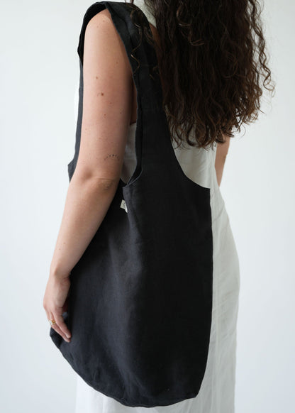 A woman wearing a white sleeveless dress carries a large black canvas shoulder tote bag against a plain white background.