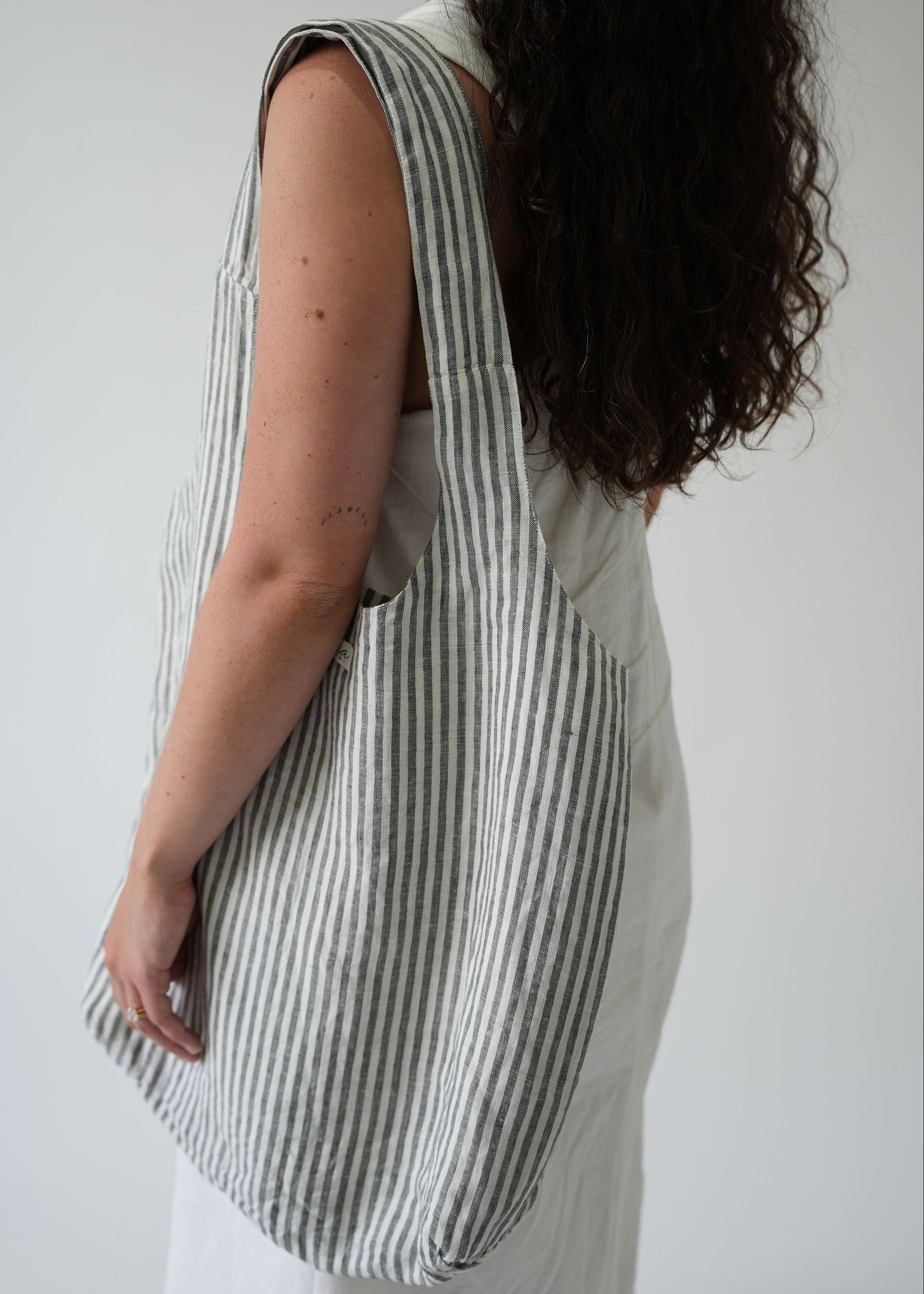 A woman shown from the back wearing a large gray and white striped fabric tote bag over her shoulder, against a plain light gray background.