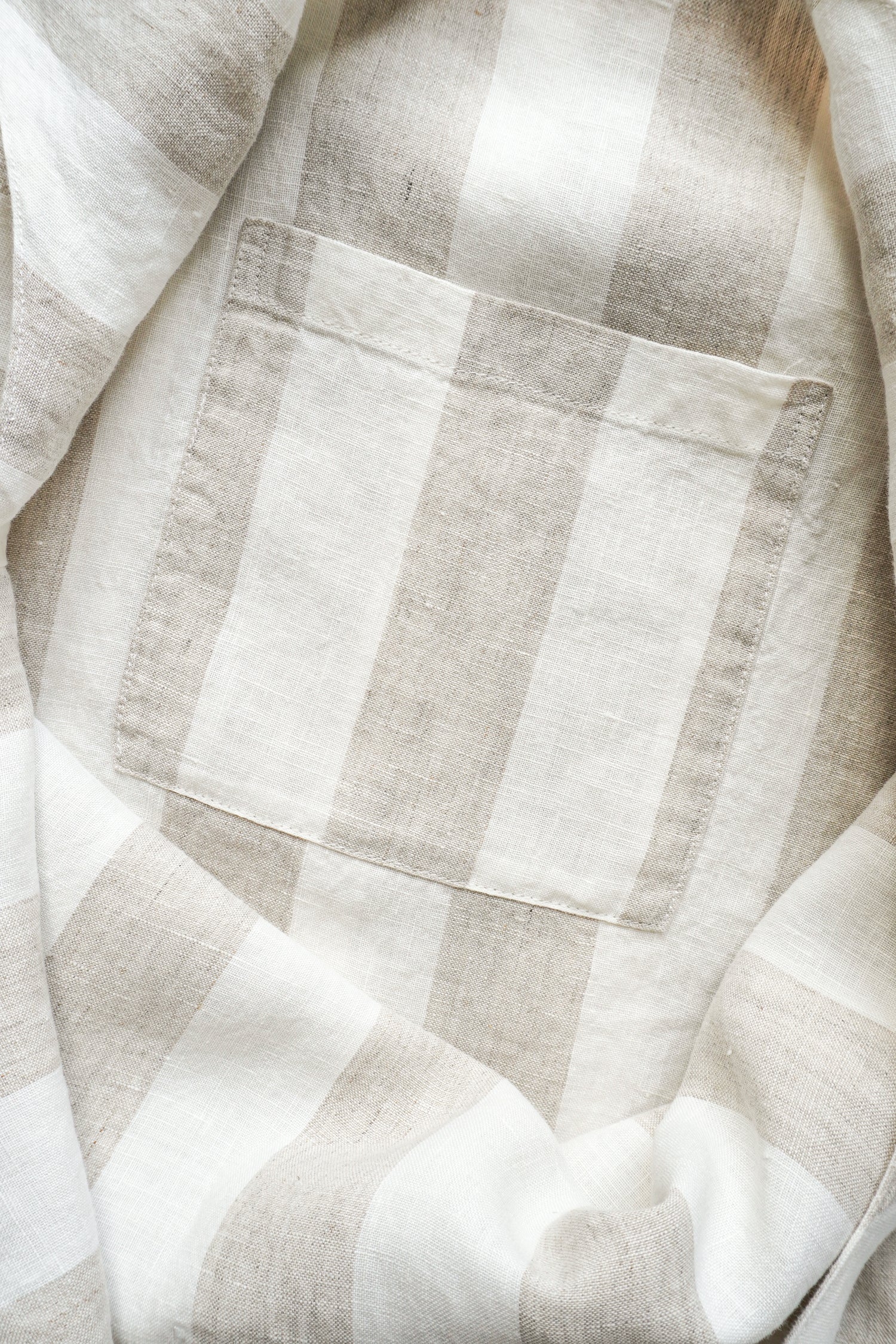 A close-up of a light beige and white striped linen fabric with a single stitched pocket.