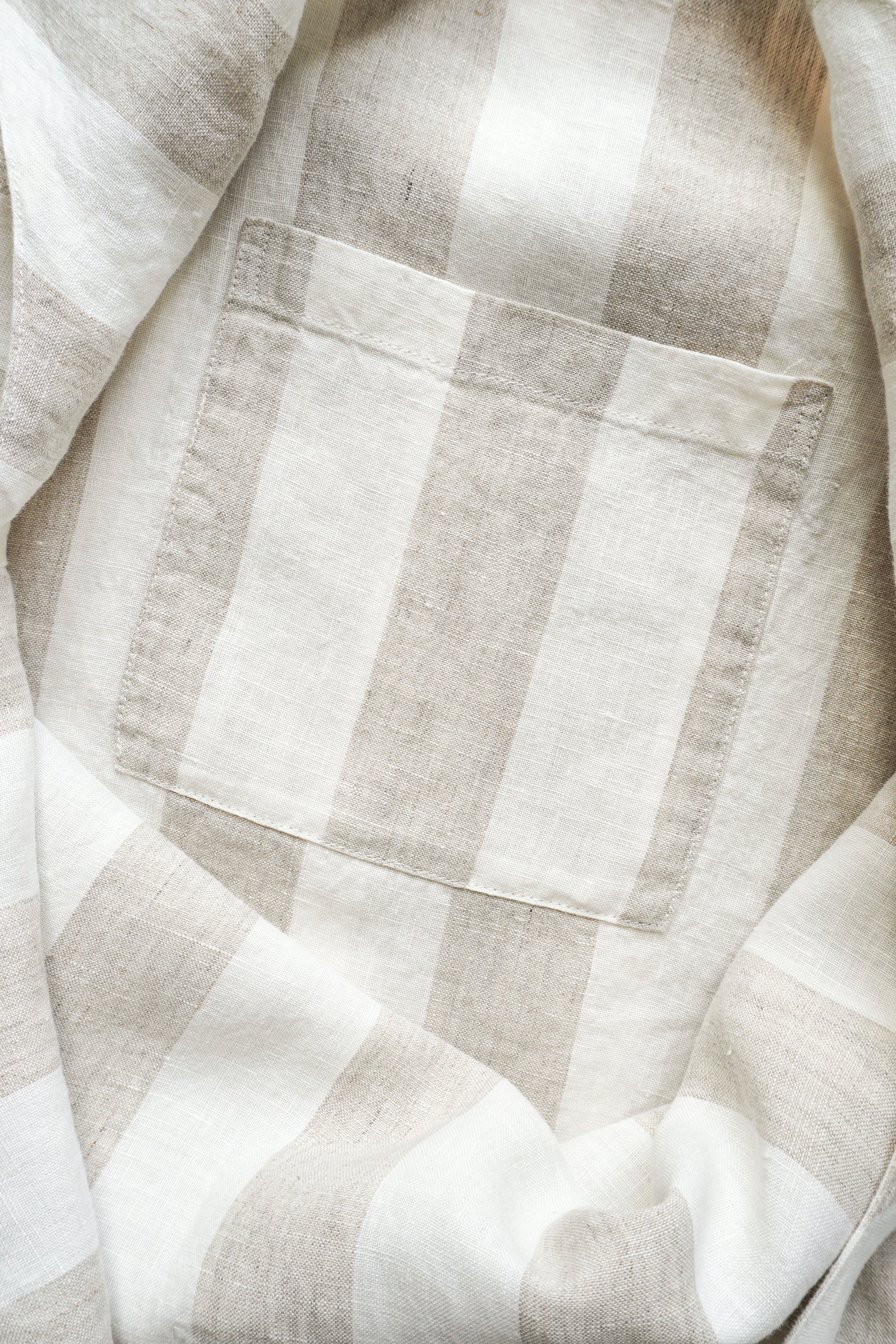 A close-up of a light beige and white striped linen fabric with a single stitched pocket.