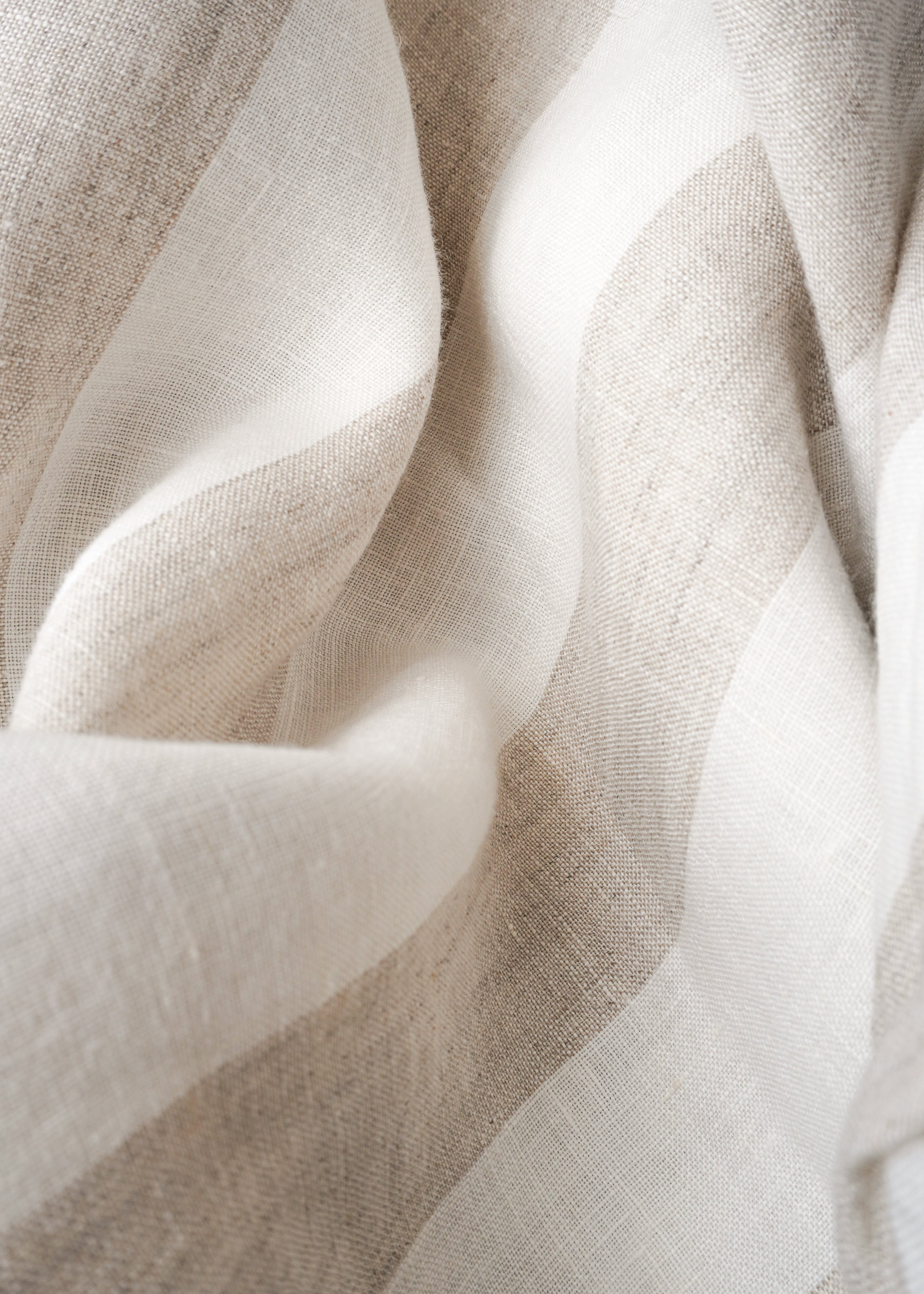 A close-up of draped fabric with soft horizontal stripes in off-white and light beige, showing a fine woven texture.