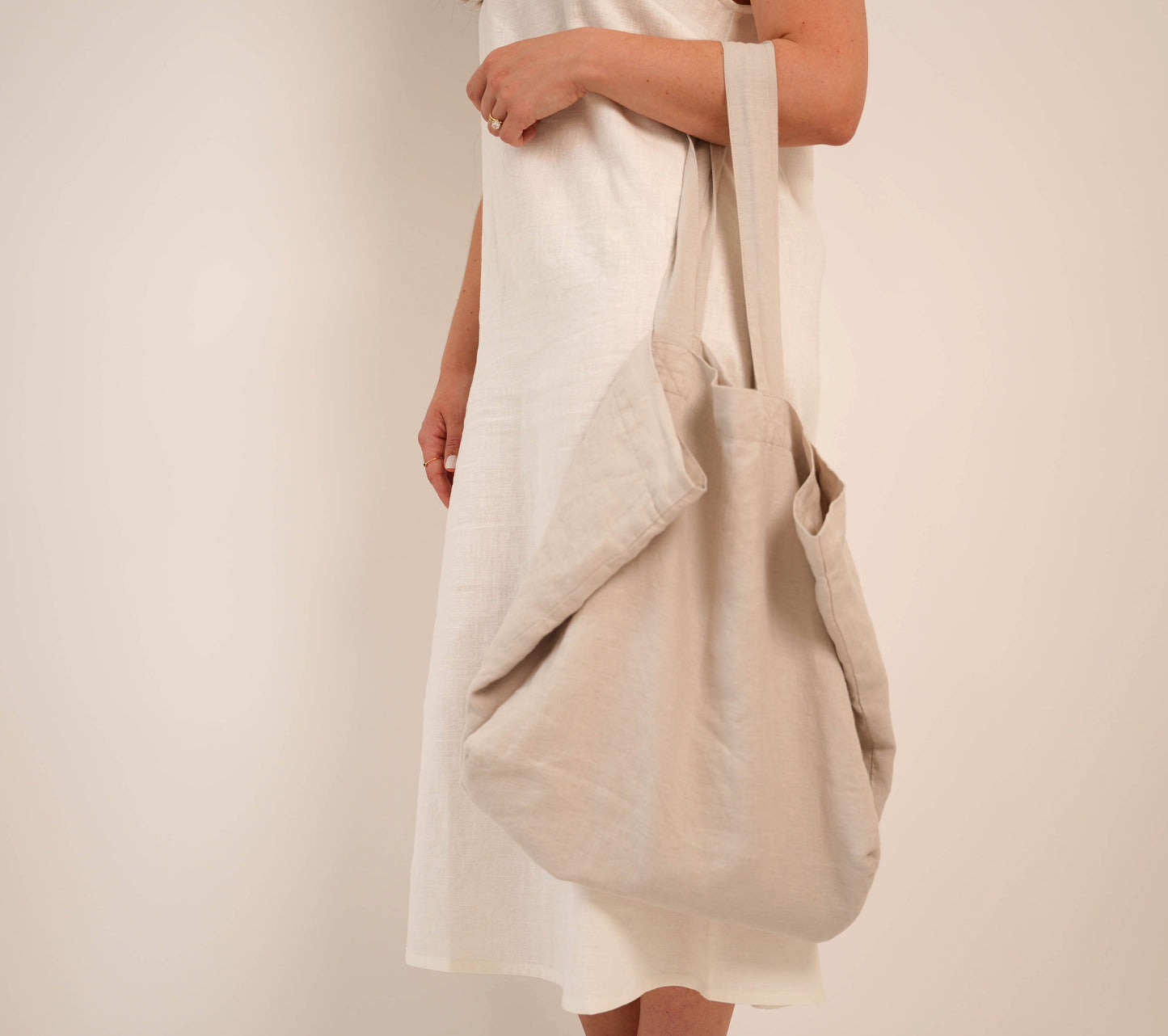 Close-up of woman carrying oversized natural linen tote bag over shoulder, white studio background — Lúa Miami