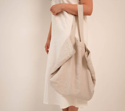 Close-up of woman carrying oversized natural linen tote bag over shoulder, white studio background — Lúa Miami