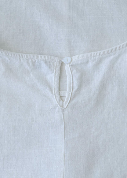 A close-up of a white sleeveless top or dress laid flat, showing the back neckline with a small button closure and stitched edge details.