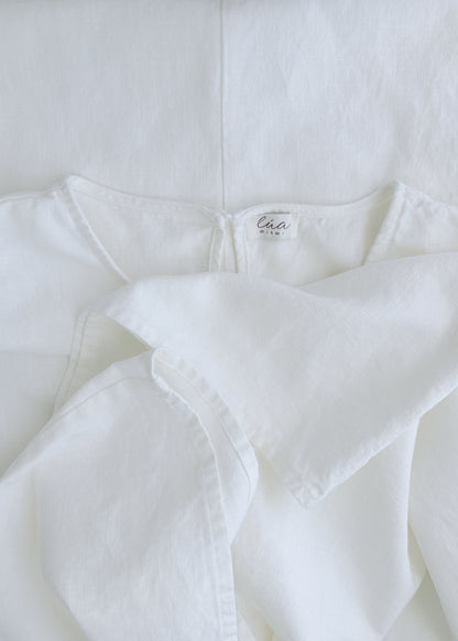 A close-up of a white cotton garment, showing the inner neck label. The fabric is softly draped, highlighting its textured, lightweight weave.