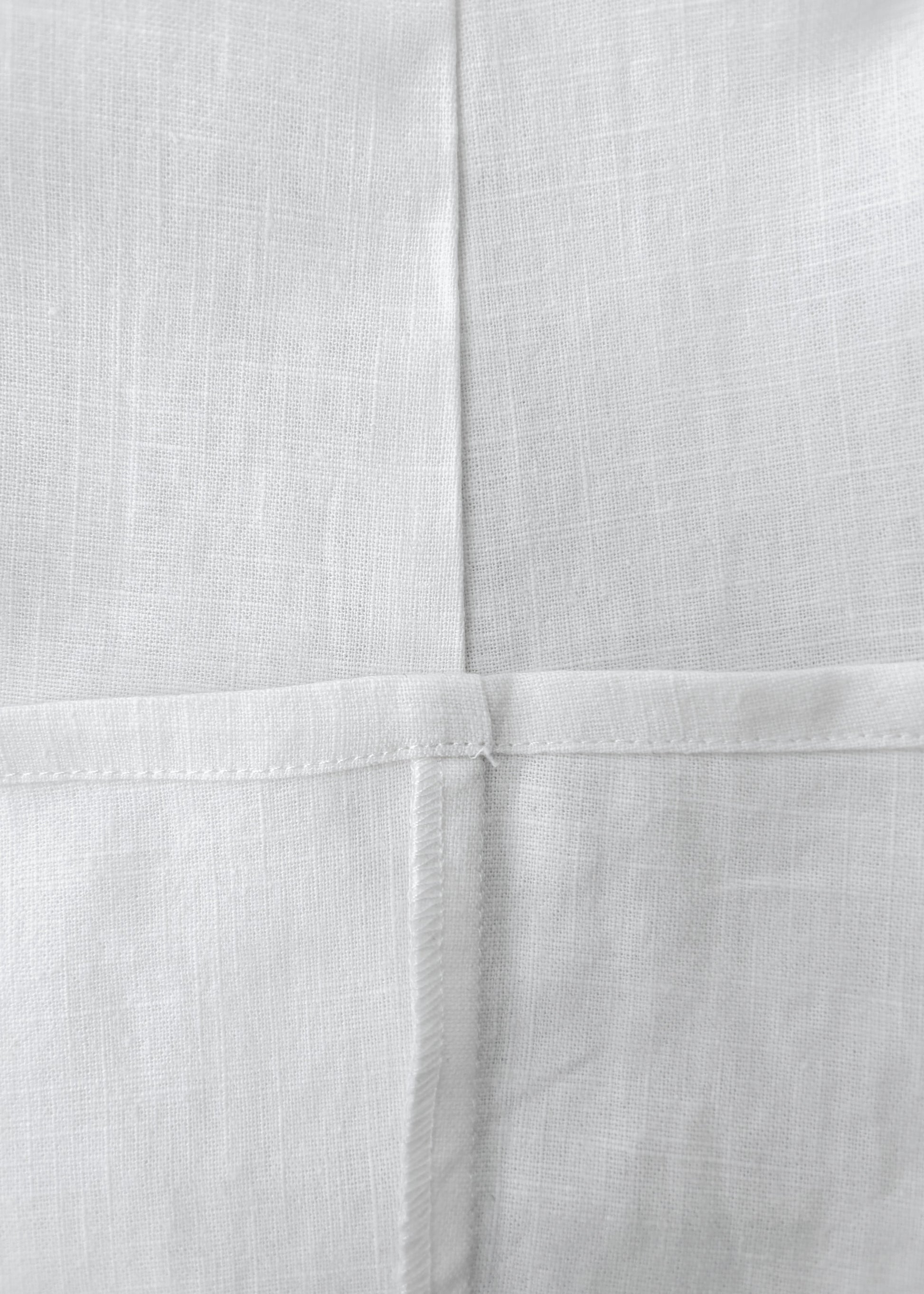 Close-up of white woven fabric with a visible cross-stitch pattern and fine linen texture.