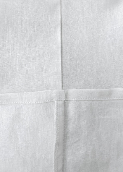 Close-up of white woven fabric with a visible cross-stitch pattern and fine linen texture.