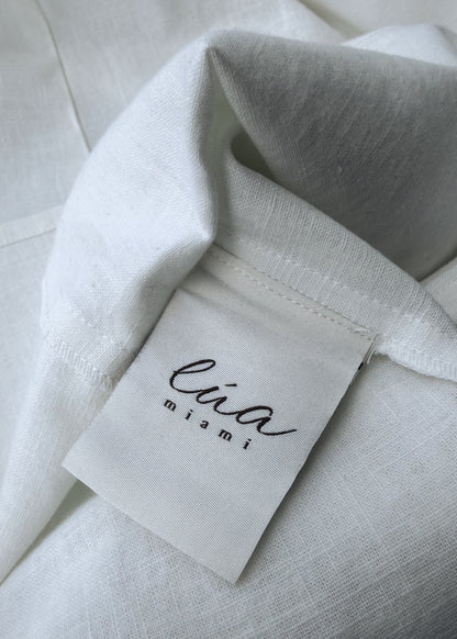 Close-up of a white textured fabric garment with a sewn-on fabric label reading 'lua miami' in black script.