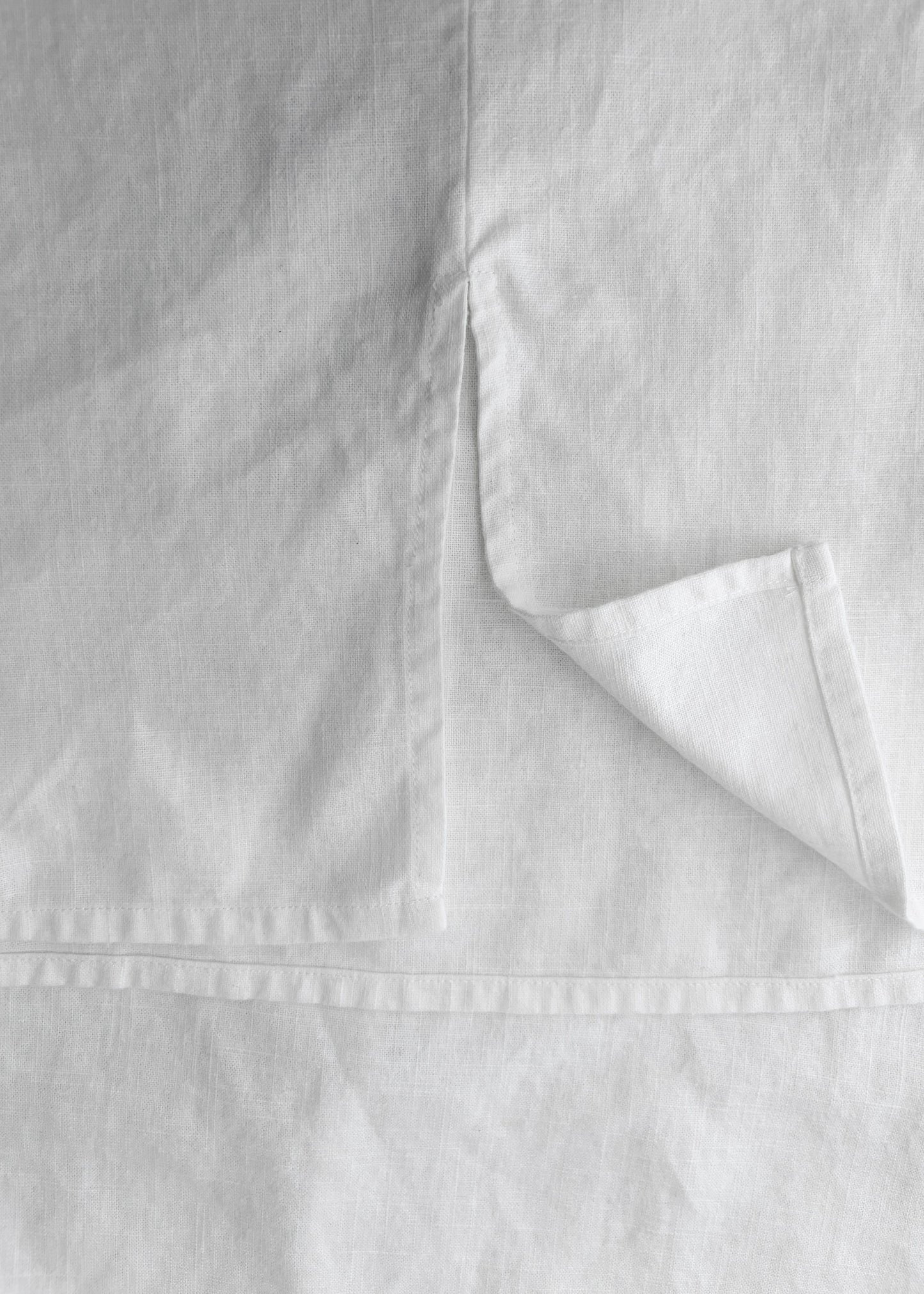 Close-up of white linen fabric with a folded corner showing the texture and hem detail.