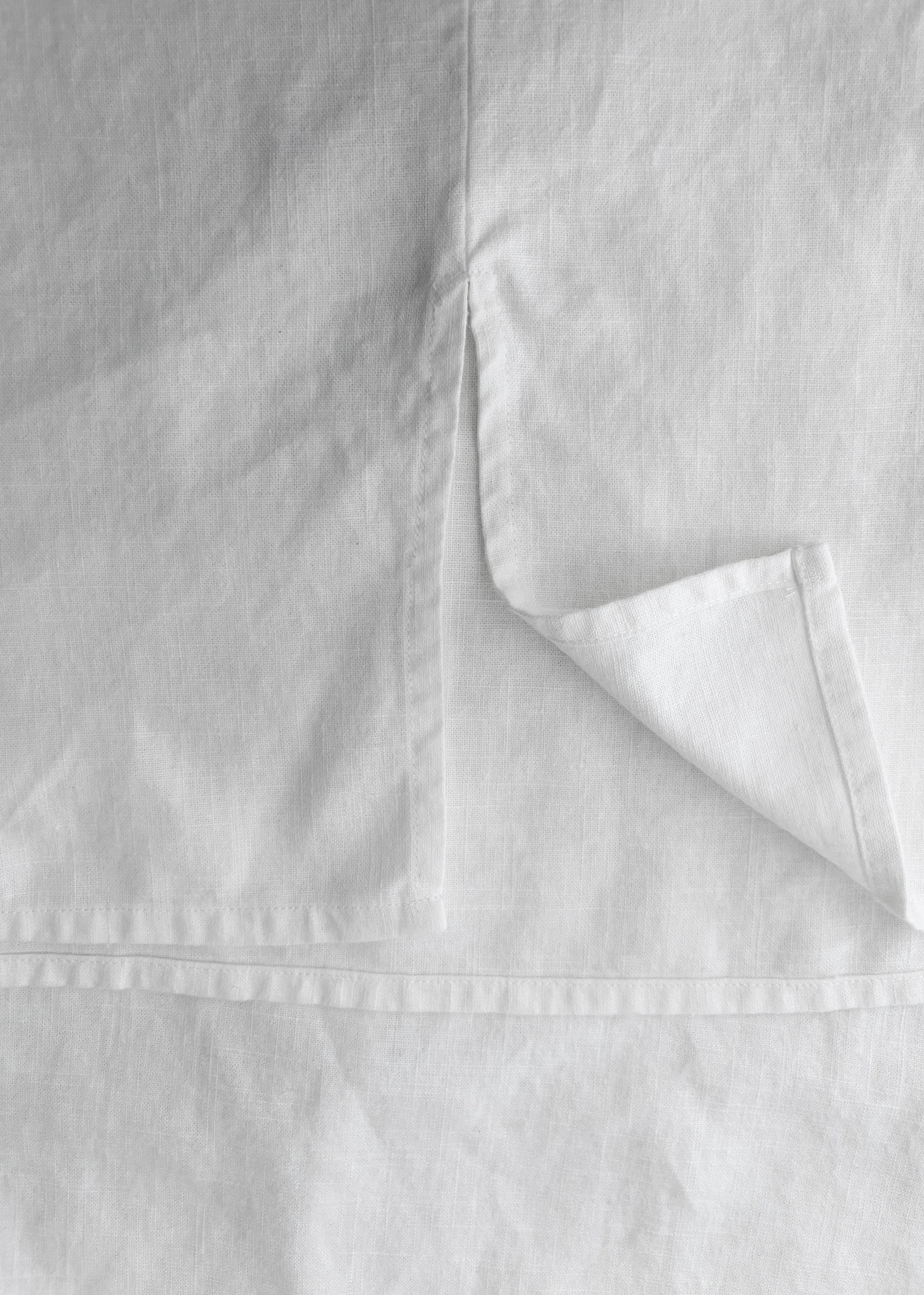 Close-up of white linen fabric with a folded corner showing the texture and hem detail.
