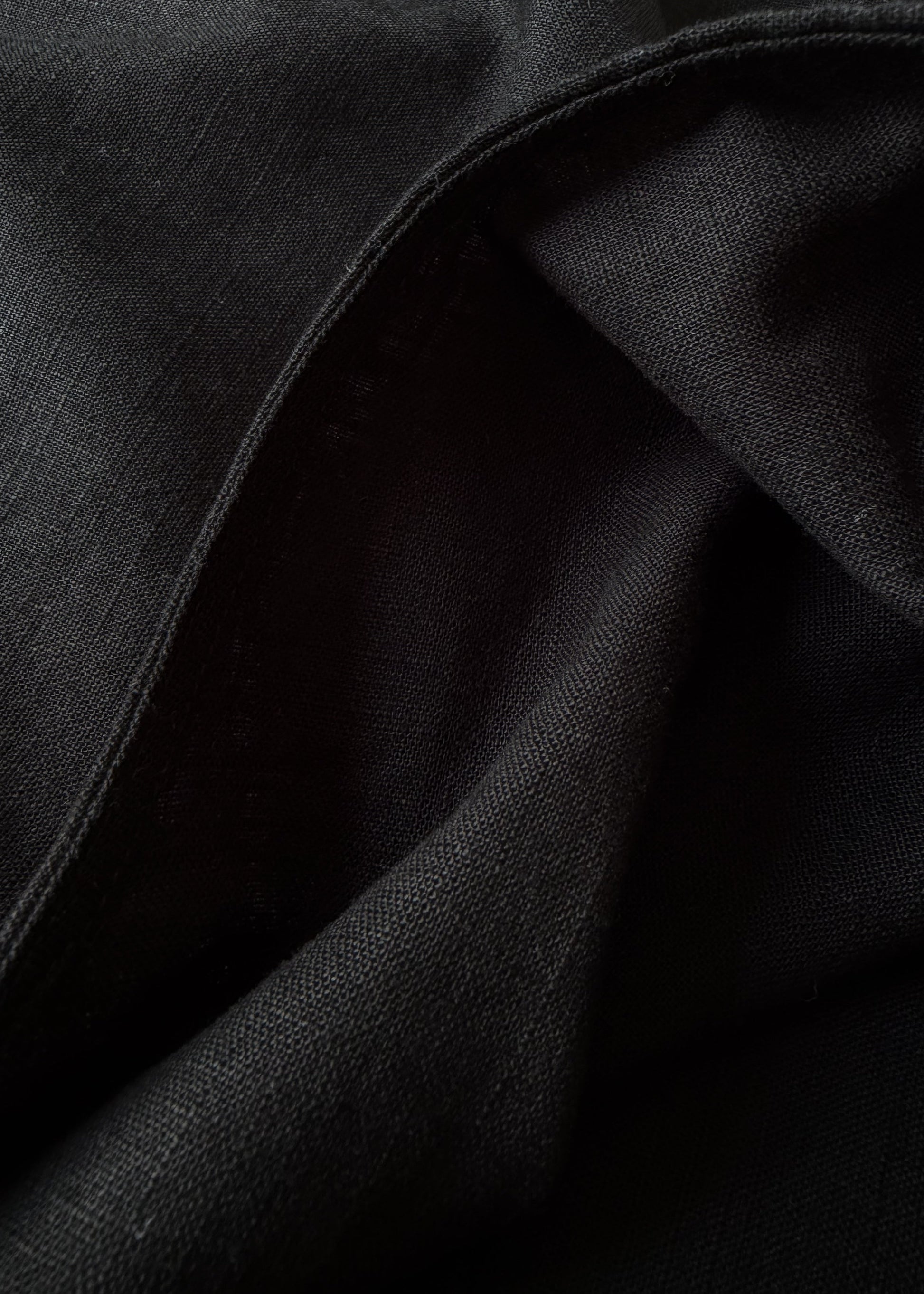 A close-up of draped black fabric with visible woven texture and soft folds.