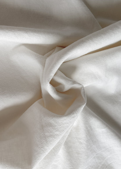 A close-up of draped off-white fabric with soft folds and a slightly warm, cream tone.