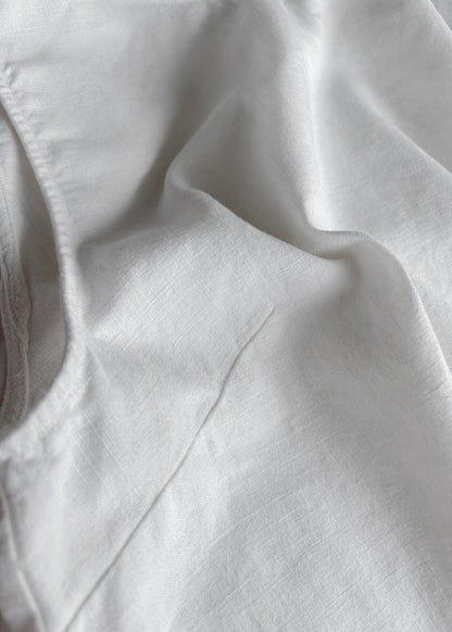A close-up of white fabric with soft folds and a visible stitched edge on the left side.