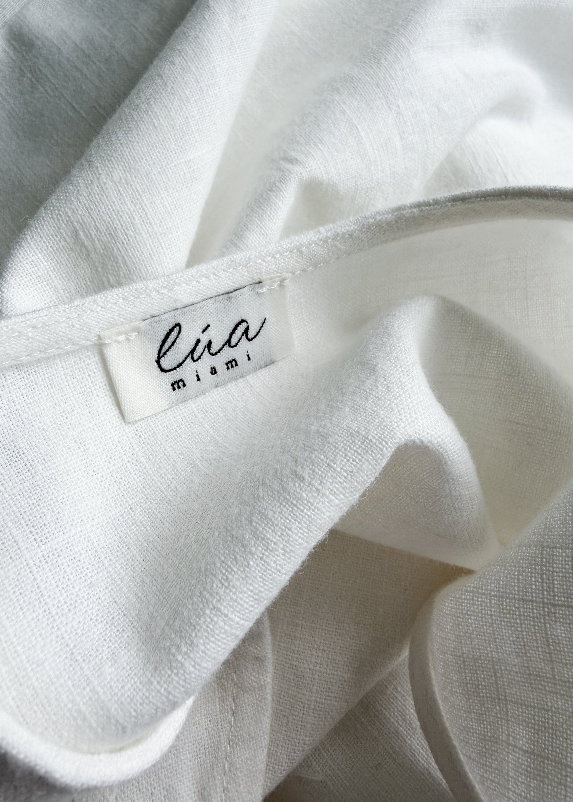 Close-up of a white textured fabric product with a sewn-in label reading 'lua miami'.